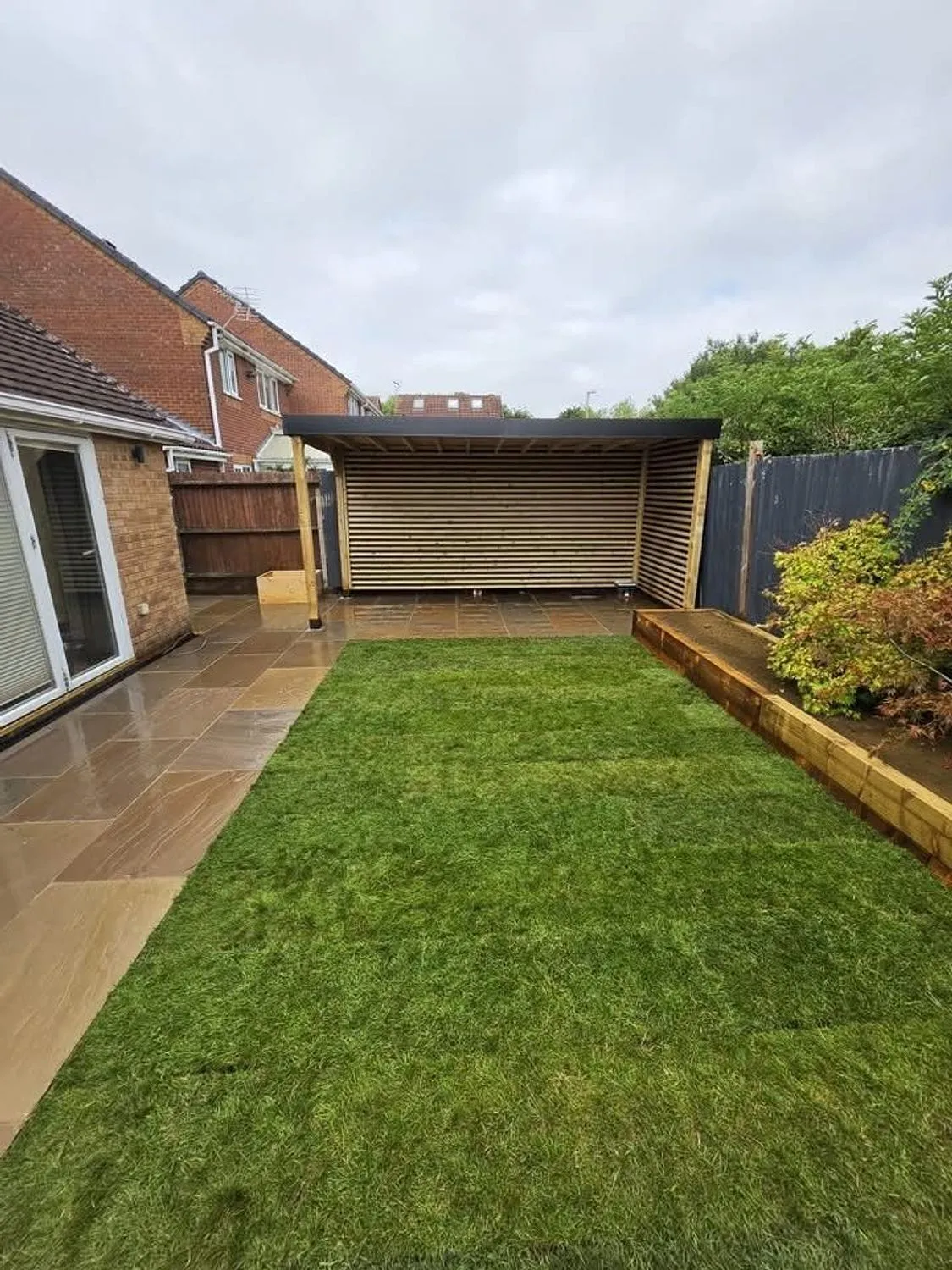 Finished rear garden with sandstone paving, new lawn and a slatted timber structure