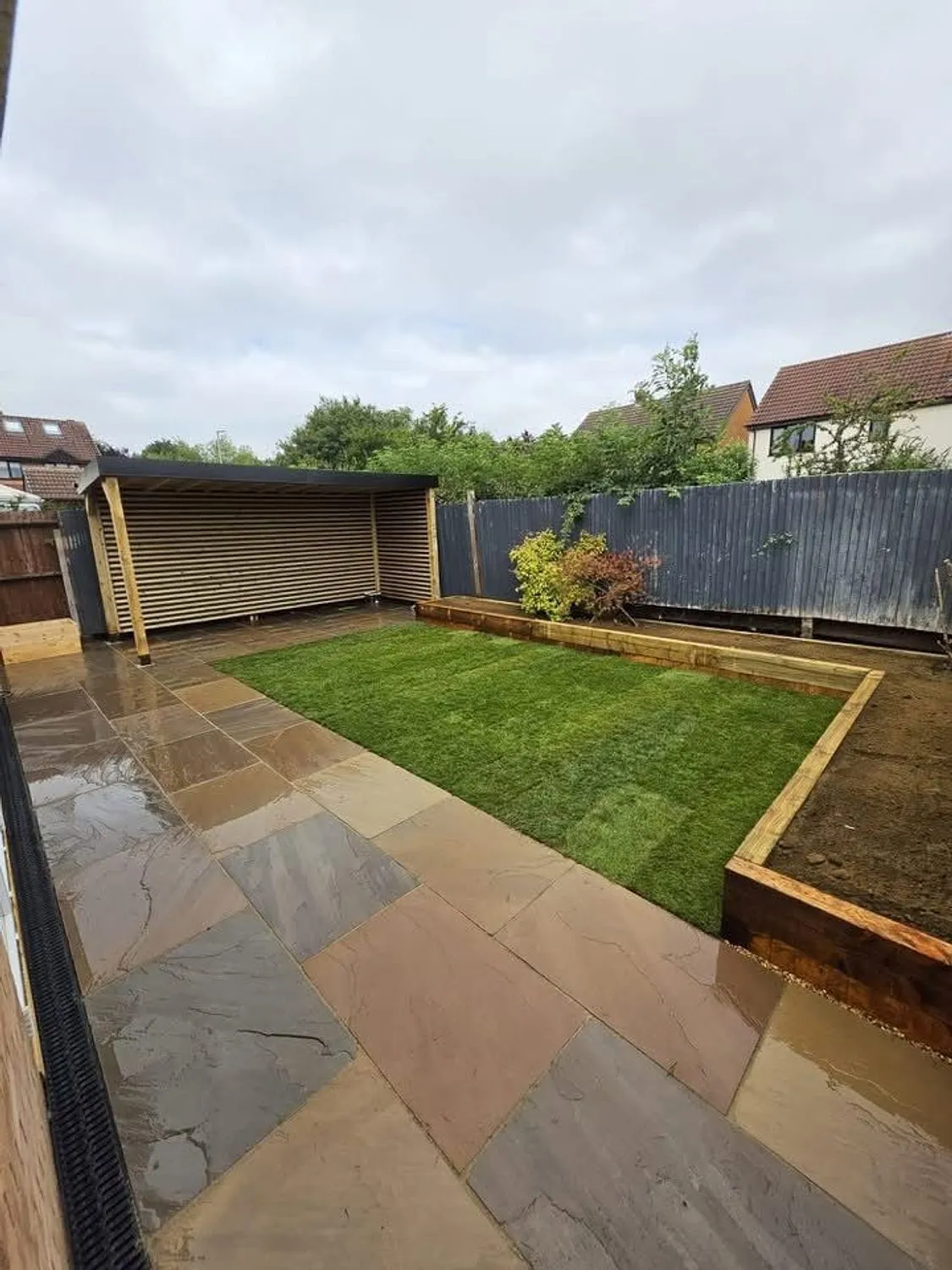 Finished garden with sleeper planters, sandstone paving and a covered seating area