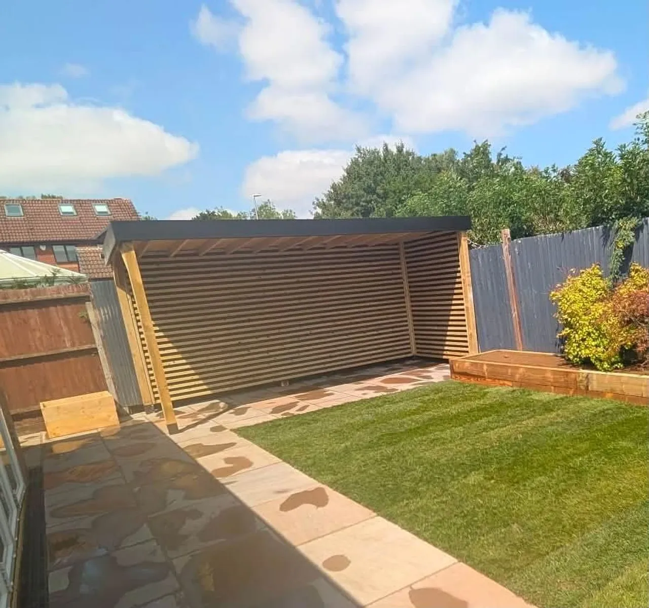 Slatted timber garden structure and sandstone paving in a completed rear garden