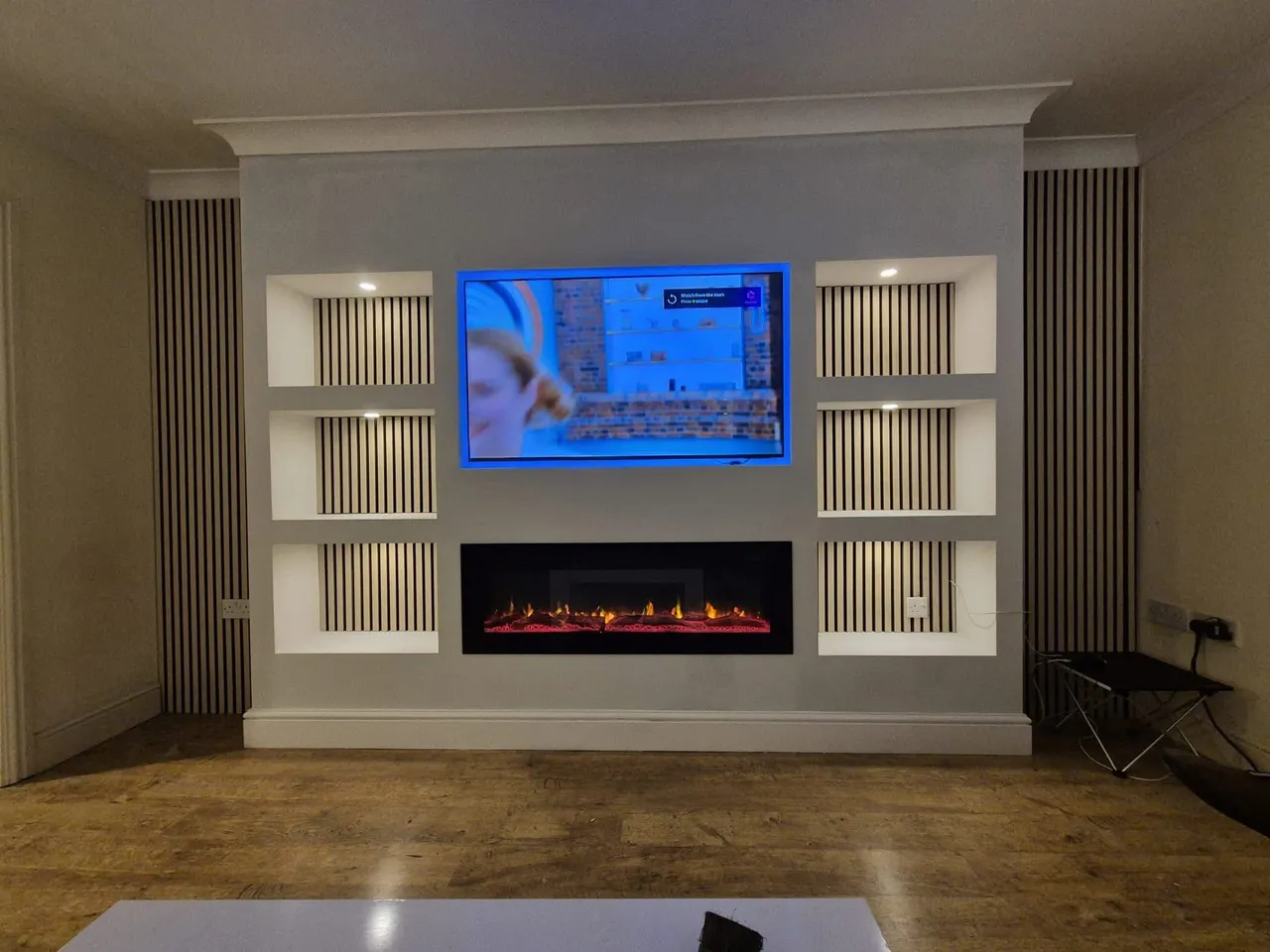 Finished media wall with a fitted electric fire, slatted panels and lit recesses