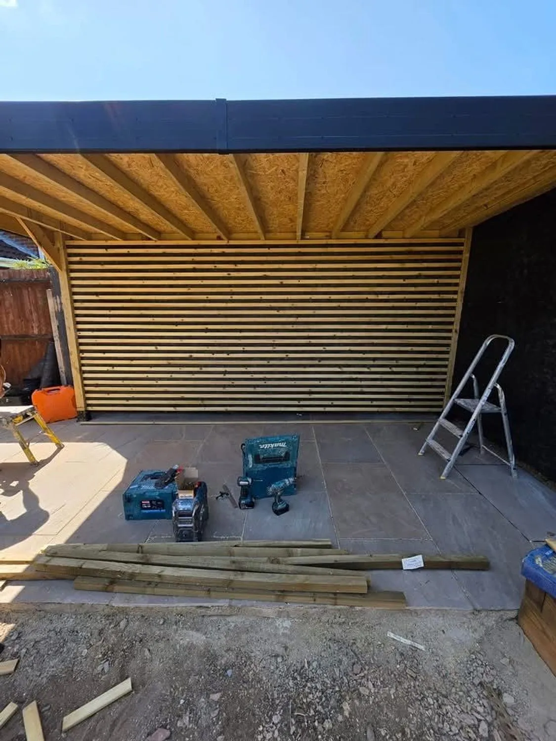 Slatted timber garden structure with an exposed rafter roof under construction